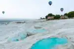 Scenic view of Pamukkale's white travertine terraces with turquoise pools and hot air balloons soaring above.