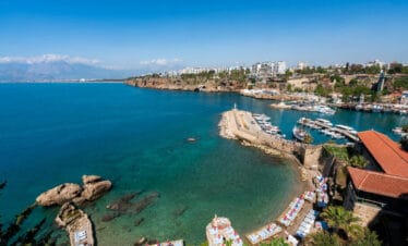 Stunning view of Antalya Old Harbor, Turkey, with clear turquoise waters, boats, cliffs, and beach loungers along the Mediterranean coast.