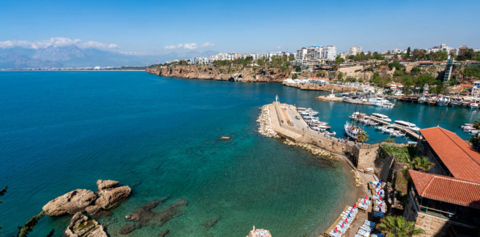 Stunning view of Antalya Old Harbor, Turkey, with clear turquoise waters, boats, cliffs, and beach loungers along the Mediterranean coast.