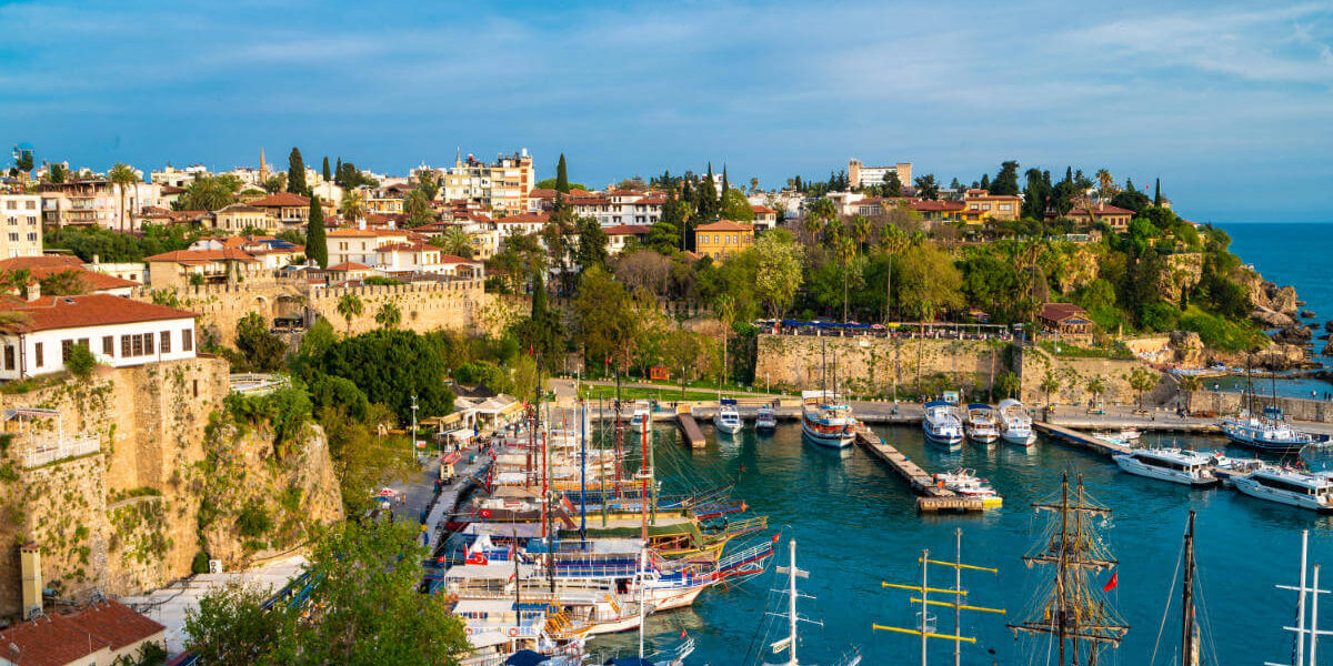 Boats docked in Antalya Kaleiçi Marina with historic Old Town houses and ancient stone walls in the background.