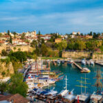 Boats docked in Antalya Kaleiçi Marina with historic Old Town houses and ancient stone walls in the background.