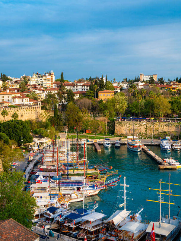 Boats docked in Antalya Kaleiçi Marina with historic Old Town houses and ancient stone walls in the background.