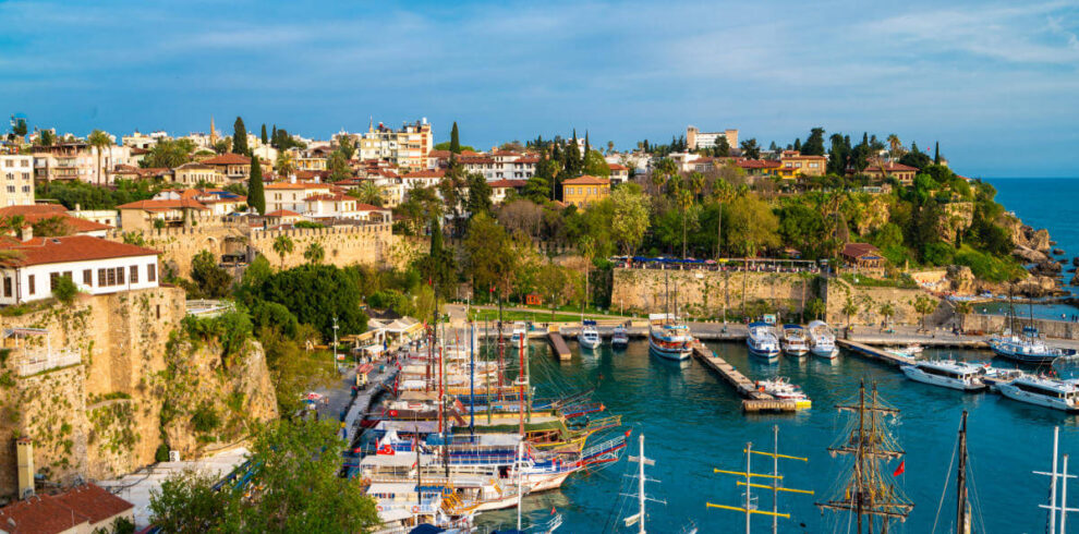 Boats docked in Antalya Kaleiçi Marina with historic Old Town houses and ancient stone walls in the background.