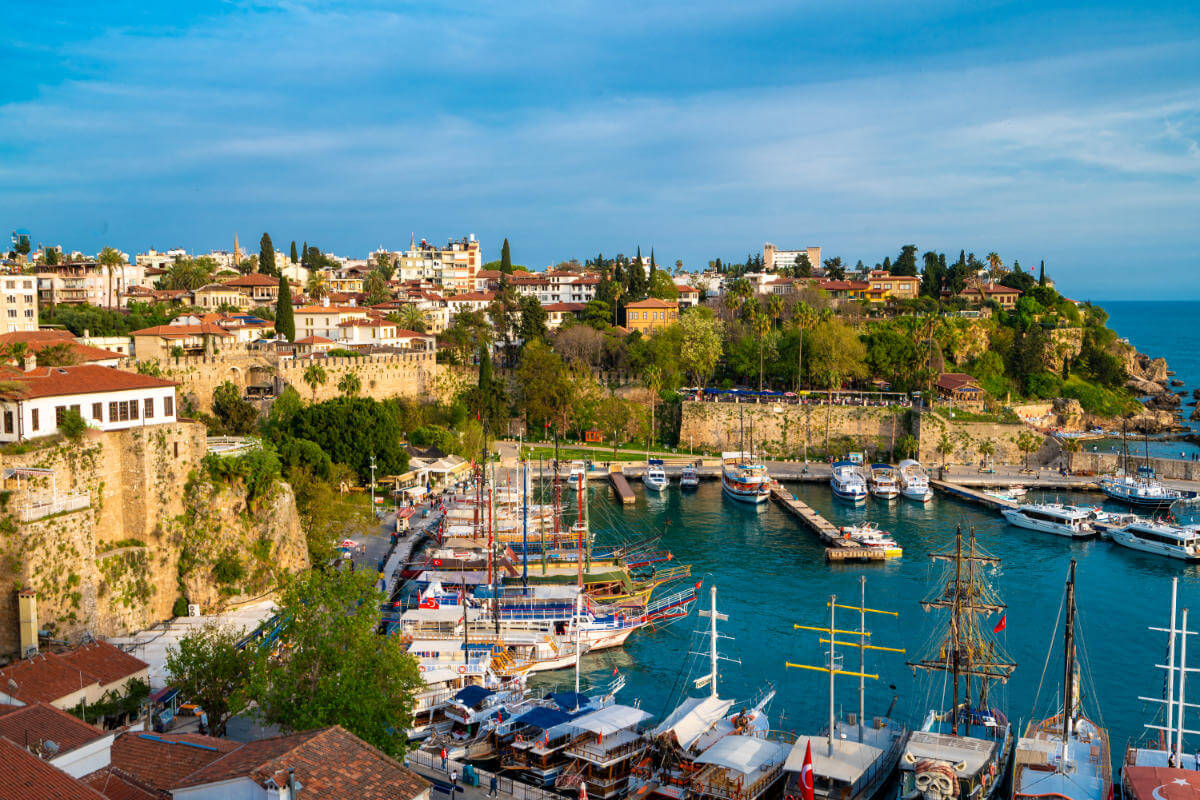 Boats docked in Antalya Kaleiçi Marina with historic Old Town houses and ancient stone walls in the background.