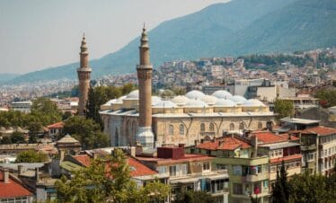 Ulu Cami mosque with twin minarets surrounded by Bursa city buildings and green mountain backdrop