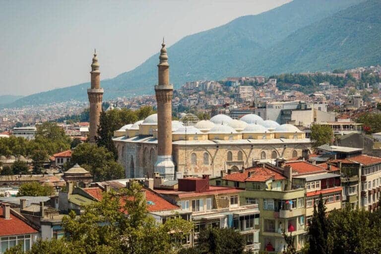 Ulu Cami mosque with twin minarets surrounded by Bursa city buildings and green mountain backdrop