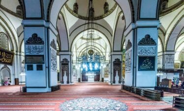 Ornate interior of Ulu Cami in Bursa featuring Islamic calligraphy, arched ceilings, and elegant chandeliers