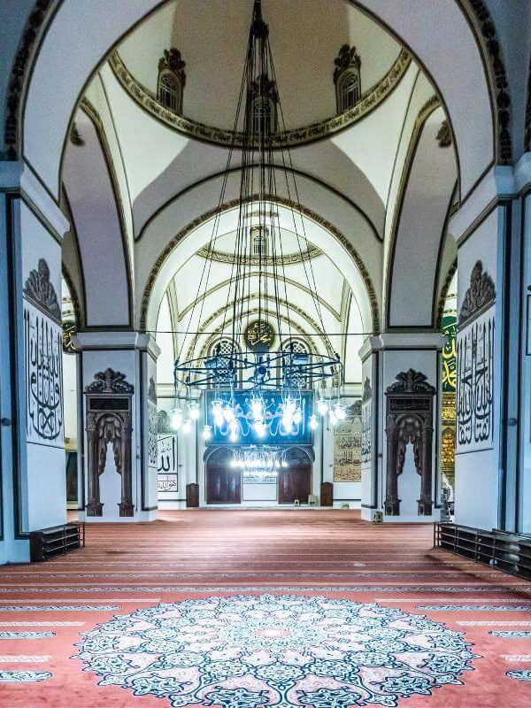 Ornate interior of Ulu Cami in Bursa featuring Islamic calligraphy, arched ceilings, and elegant chandeliers