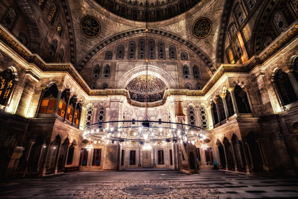Grand chandelier and intricate dome details inside an illuminated Ottoman-era mosque in Istanbul, Turkey.