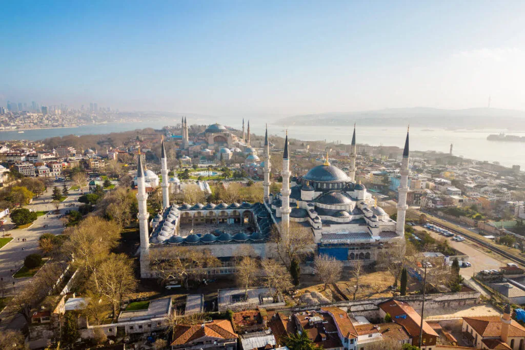 Panoramic aerial view of the Blue Mosque and Hagia Sophia with minarets and Bosphorus backdrop in Istanbul, Turkey.