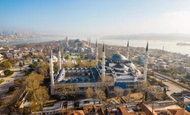 Panoramic aerial view of the Blue Mosque and Hagia Sophia with minarets and Bosphorus backdrop in Istanbul, Turkey.