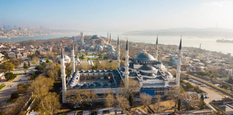 Panoramic aerial view of the Blue Mosque and Hagia Sophia with minarets and Bosphorus backdrop in Istanbul, Turkey.