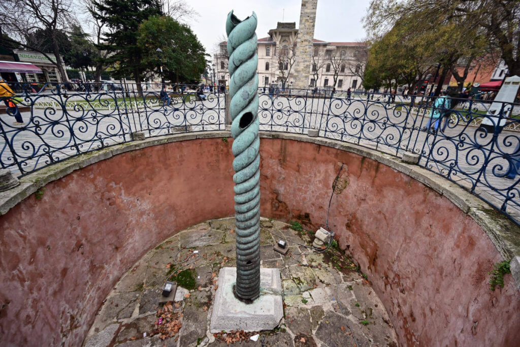 Ancient bronze Serpent Column in Sultanahmet Square, Istanbul, Turkey, set between historic landmarks and paved plaza.