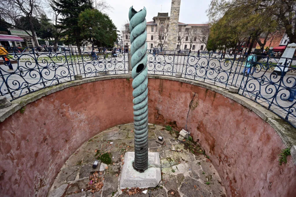 Ancient bronze Serpent Column in Sultanahmet Square, Istanbul, Turkey, set between historic landmarks and paved plaza.