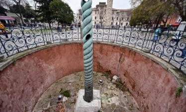 Ancient bronze Serpent Column in Sultanahmet Square, Istanbul, Turkey, set between historic landmarks and paved plaza.
