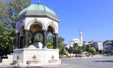 Ornate German Fountain with green dome and marble base in Sultanahmet Square, Istanbul, on a sunny day.