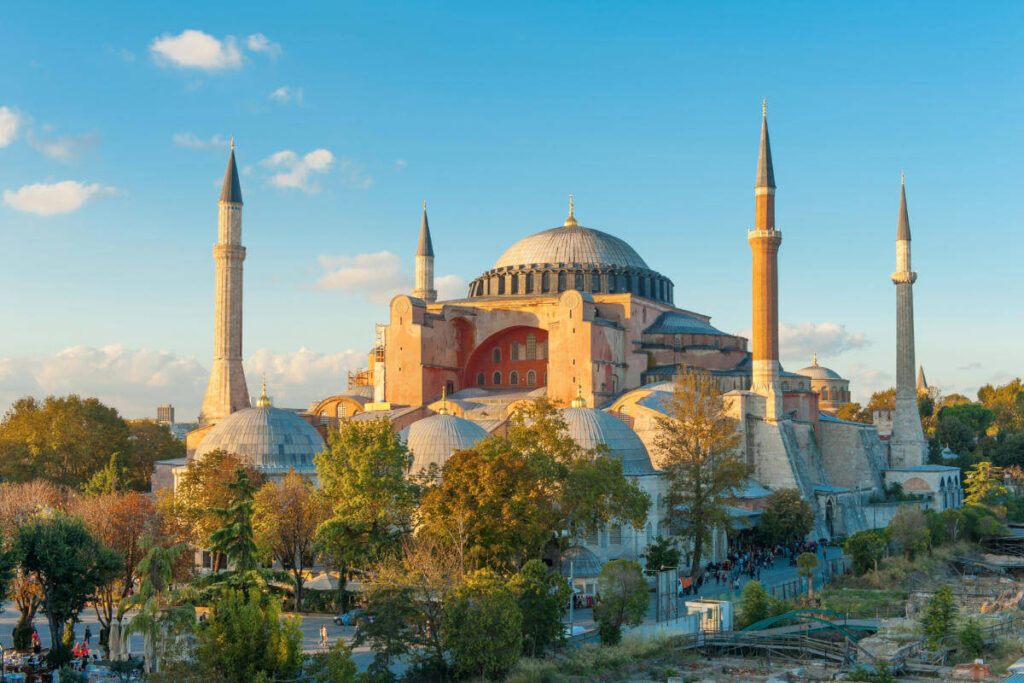 Hagia Sophia bathed in golden hour light with domes and minarets rising above trees in Istanbul, Turkey.