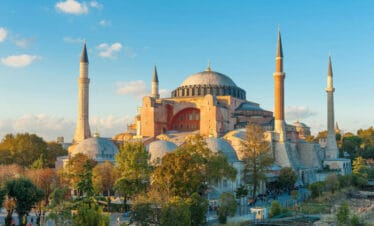 Hagia Sophia bathed in golden hour light with domes and minarets rising above trees in Istanbul, Turkey.