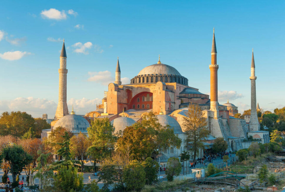Hagia Sophia bathed in golden hour light with domes and minarets rising above trees in Istanbul, Turkey.
