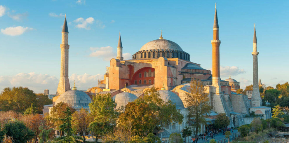 Hagia Sophia bathed in golden hour light with domes and minarets rising above trees in Istanbul, Turkey.