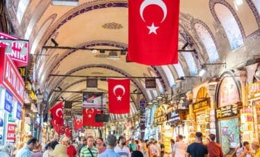Shoppers browse vibrant stalls under arched ceilings with Turkish flags in Istanbul’s historic Grand Bazaar.