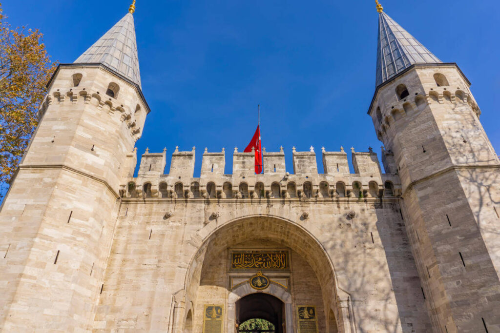 Historic main gate of Topkapi Palace in Istanbul with twin towers and Ottoman architectural design under blue sky.