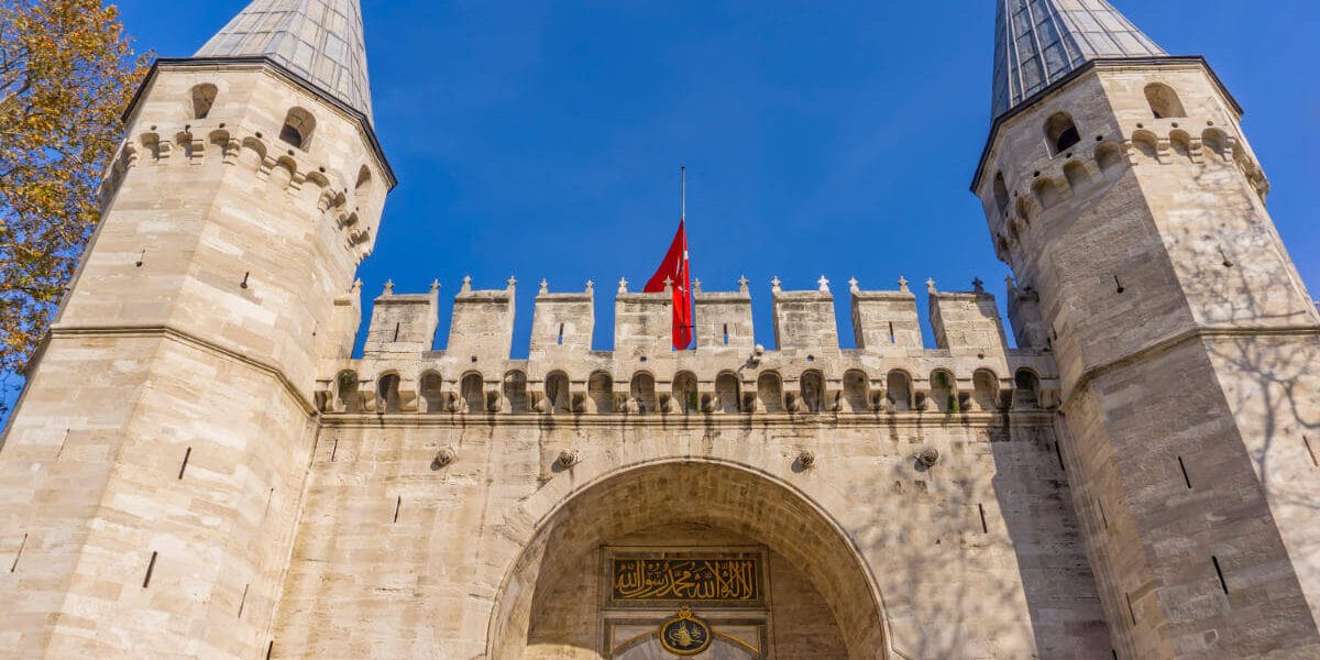 Historic main gate of Topkapi Palace in Istanbul with twin towers and Ottoman architectural design under blue sky.