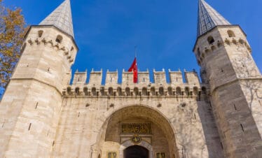 Historic main gate of Topkapi Palace in Istanbul with twin towers and Ottoman architectural design under blue sky.