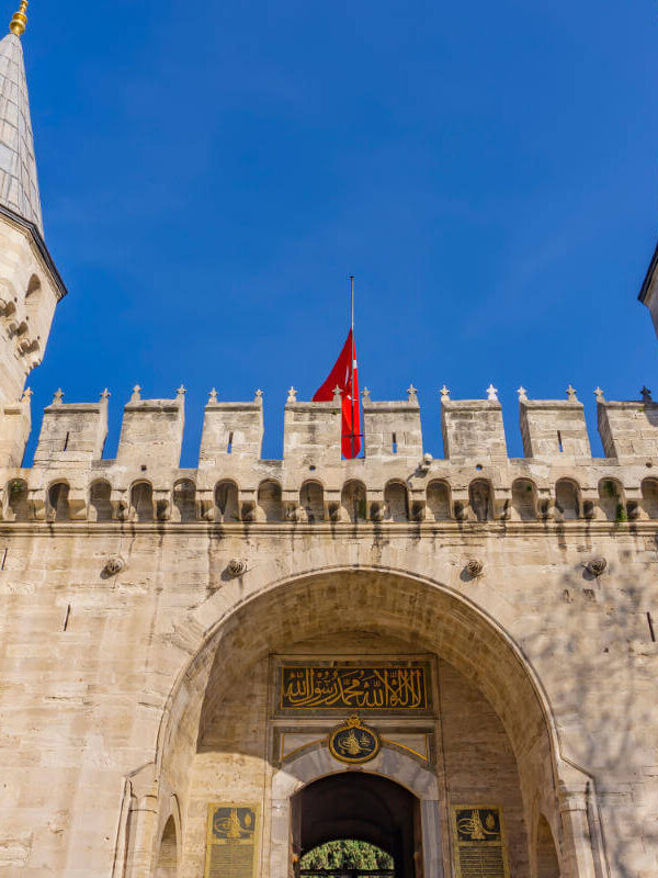 Historic main gate of Topkapi Palace in Istanbul with twin towers and Ottoman architectural design under blue sky.