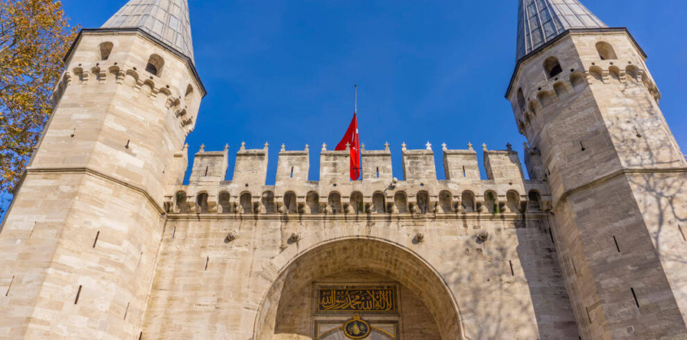 Historic main gate of Topkapi Palace in Istanbul with twin towers and Ottoman architectural design under blue sky.