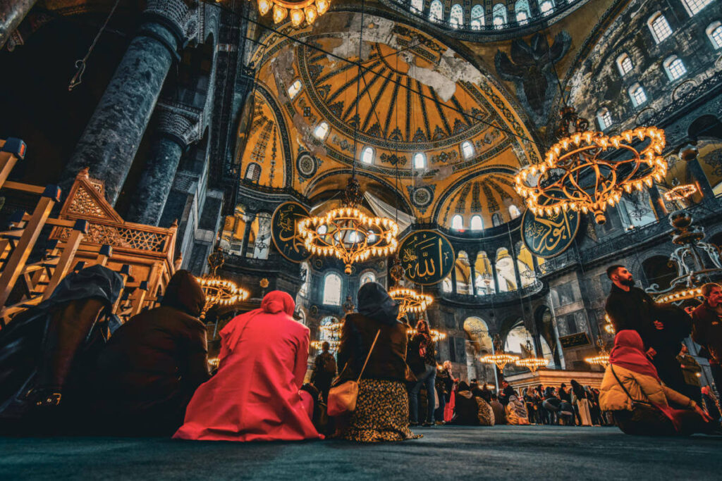 Interior of Hagia Sophia with worshippers beneath grand domes and chandeliers in historic Istanbul setting.