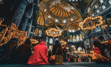Interior of Hagia Sophia with worshippers beneath grand domes and chandeliers in historic Istanbul setting.