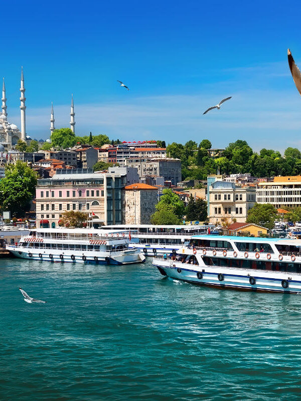Passenger ferries on the Bosphorus with Istanbul’s skyline and Suleymaniye Mosque under a clear blue sky.