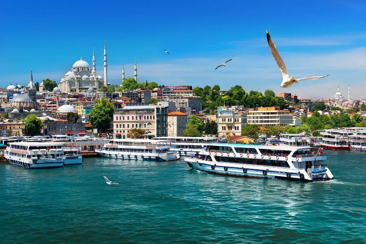 Passenger ferries on the Bosphorus with Istanbul’s skyline and Suleymaniye Mosque under a clear blue sky.