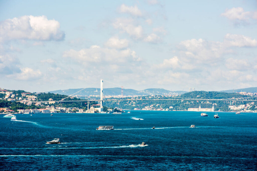 Expansive view of Istanbul's Bosphorus Strait featuring bustling boats, scenic hills, and the iconic Bosphorus Bridge on a partly cloudy day.
