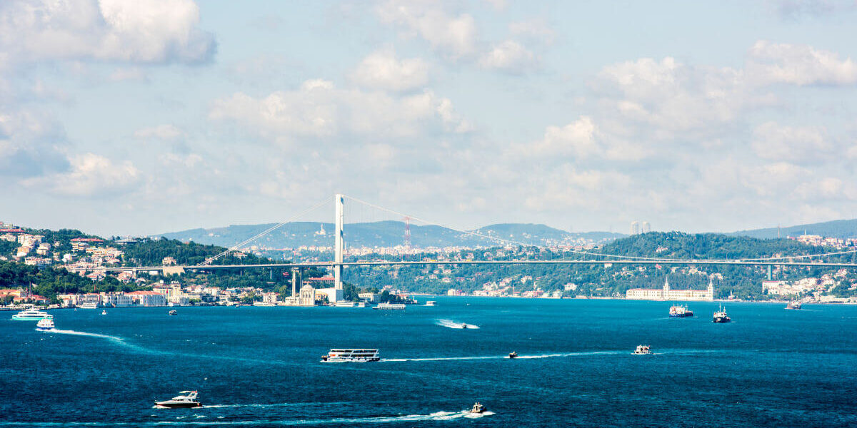 Expansive view of Istanbul's Bosphorus Strait featuring bustling boats, scenic hills, and the iconic Bosphorus Bridge on a partly cloudy day.