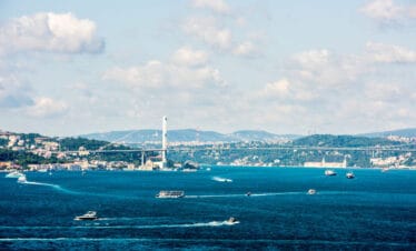 Expansive view of Istanbul's Bosphorus Strait featuring bustling boats, scenic hills, and the iconic Bosphorus Bridge on a partly cloudy day.