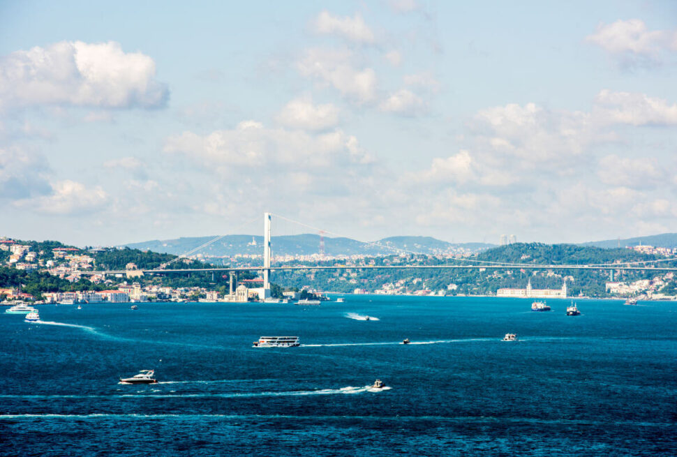 Expansive view of Istanbul's Bosphorus Strait featuring bustling boats, scenic hills, and the iconic Bosphorus Bridge on a partly cloudy day.