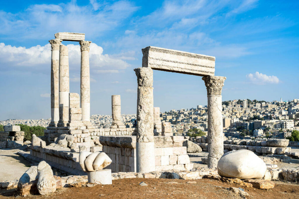 Ancient stone columns of the Temple of Hercules at Amman Citadel with cityscape in the background.