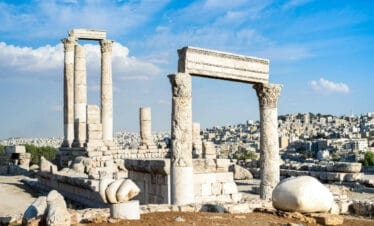 Ancient stone columns of the Temple of Hercules at Amman Citadel with cityscape in the background.