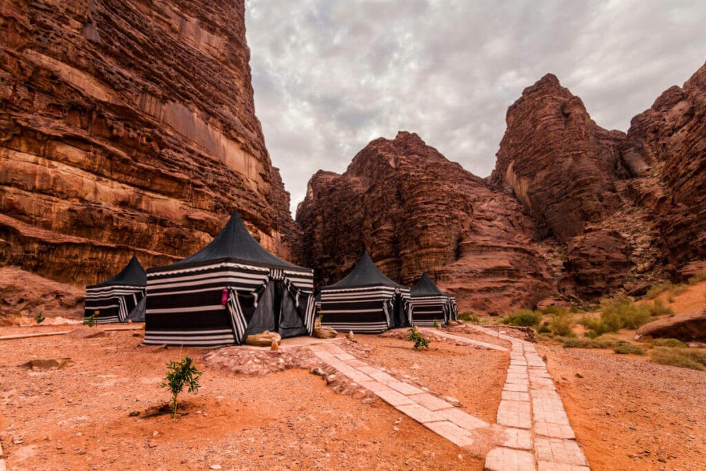Traditional Bedouin tents set in the red sandstone cliffs of Wadi Rum desert under a cloudy sky.