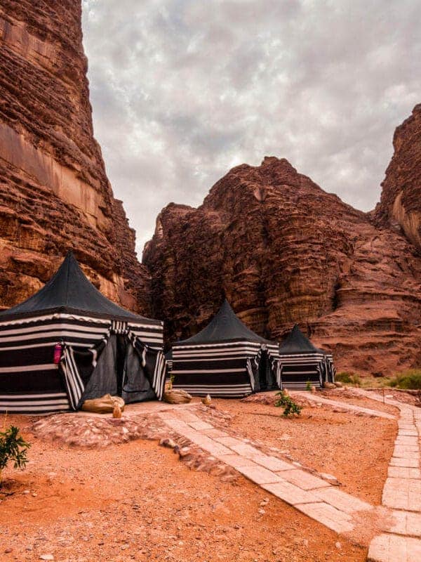 Tiendas beduinas tradicionales instaladas en los acantilados de arenisca roja del desierto de Wadi Rum bajo un cielo nublado.