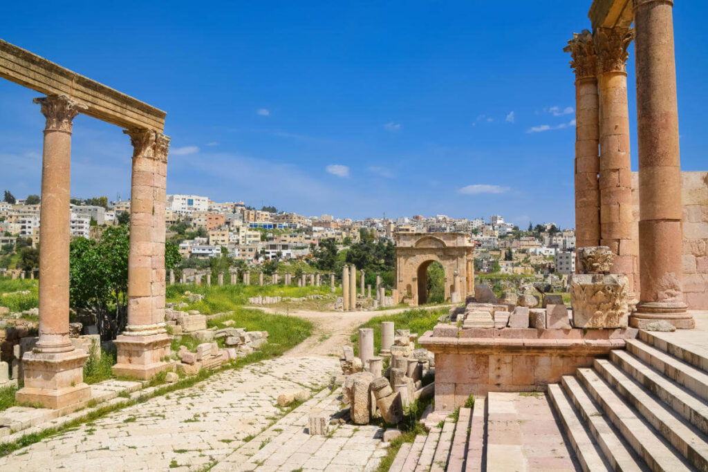 Preserved Roman columns and archways in Jerash archaeological site with modern cityscape in the background.