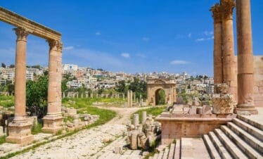 Preserved Roman columns and archways in Jerash archaeological site with modern cityscape in the background.