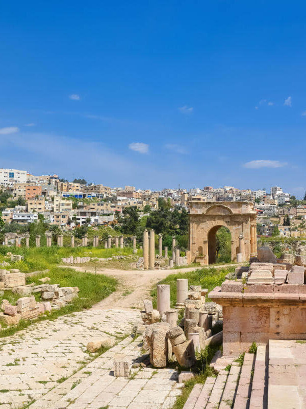 Preserved Roman columns and archways in Jerash archaeological site with modern cityscape in the background.