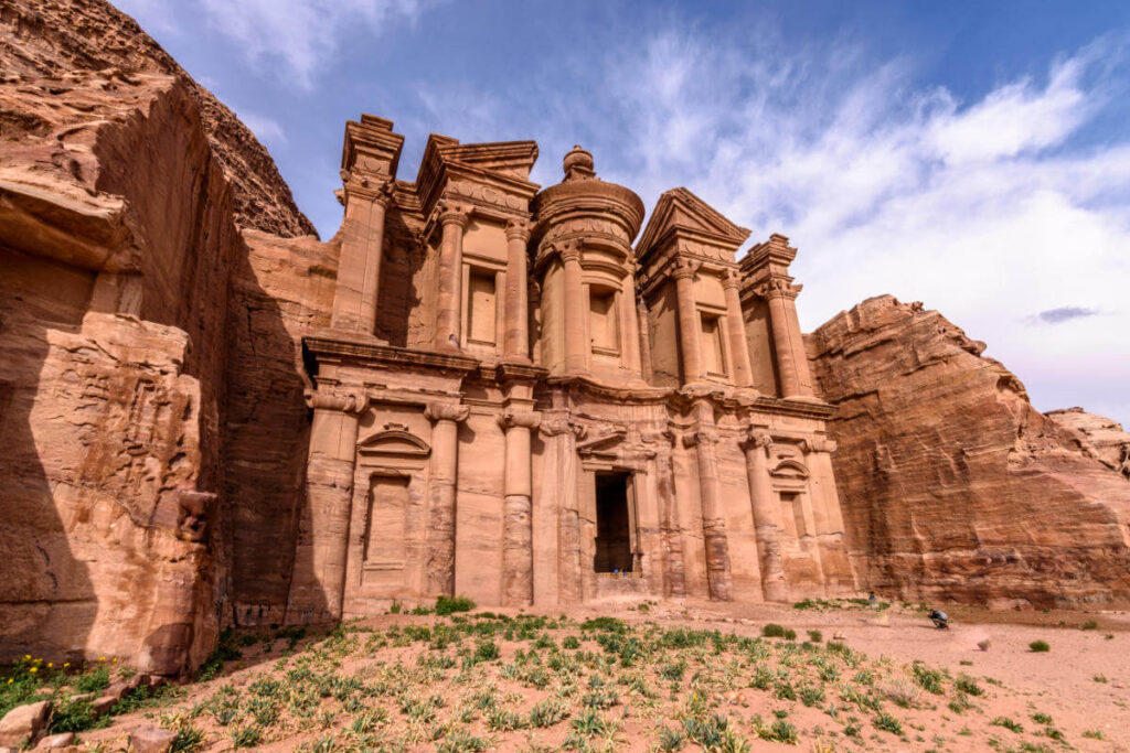 Majestic rock-carved façade of the Monastery in Petra with intricate columns and desert surroundings.