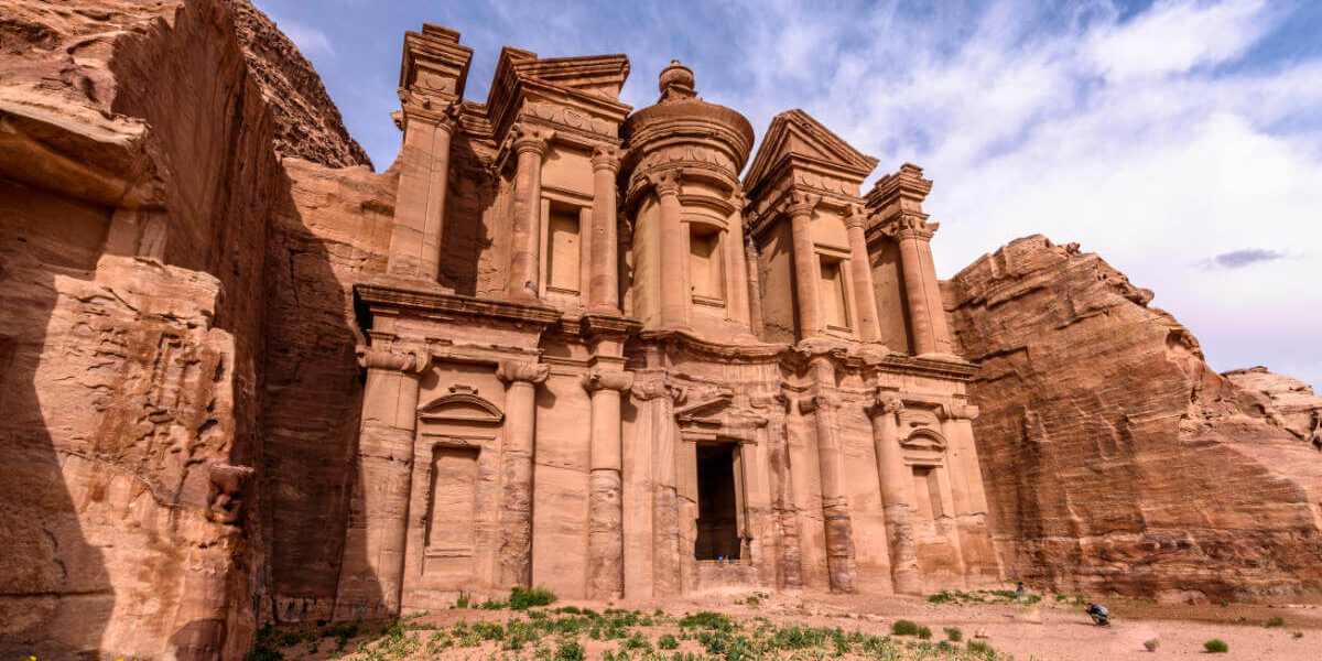 Majestic rock-carved façade of the Monastery in Petra with intricate columns and desert surroundings.