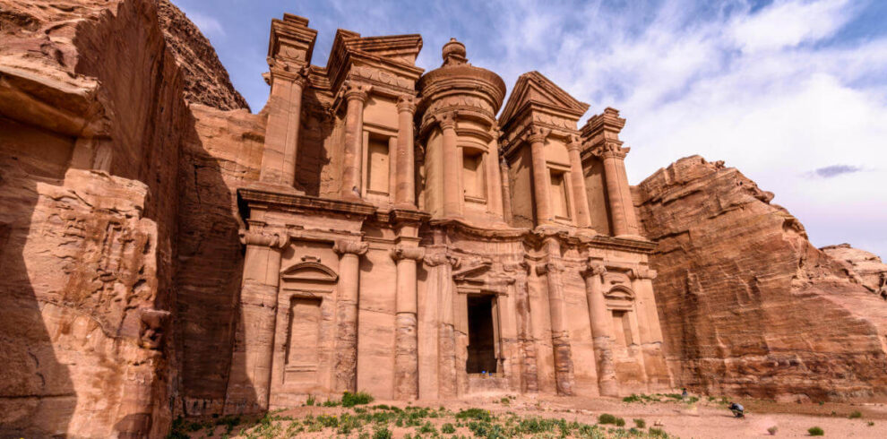 Majestic rock-carved façade of the Monastery in Petra with intricate columns and desert surroundings.