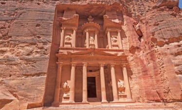 Sunlit view of Petra Treasury in Jordan, showcasing ancient sandstone carvings and detailed Nabatean architecture.