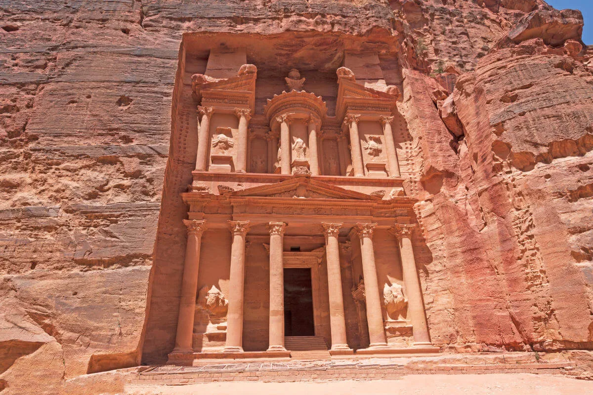 Sunlit view of Petra Treasury in Jordan, showcasing ancient sandstone carvings and detailed Nabatean architecture.